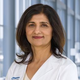 Dr. Samira Syed wearing a beige shirt and a white lab coat standing in the Clements University Hospital lobby