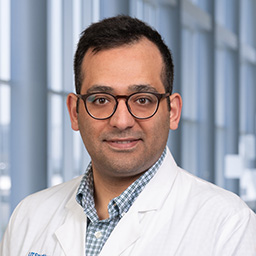 Dr. Yunus Emre Tarhan wearing a blue checkered shirt and a white lab coat standing in the Clements University Hospital lobby