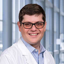 Dr. Ethan Tobias wearing a light blue shirt and a white lab coat standing in the Clements University Hospital lobby