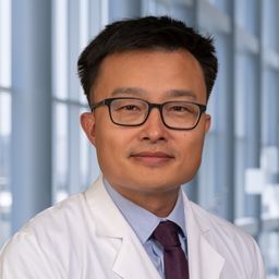 Dr. Daniel Wang wearing a blue shirt with a dark tie and a white lab coat standing in the Clements University Hospital lobby