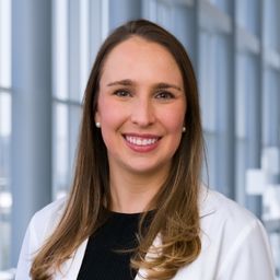Dr. Heather Wolfe wearing a black shirt and a white lab coat standing in the Clements University Hospital lobby