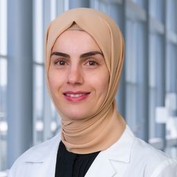 Dr. Elif Yilmaz wearing a black shirt and a white lab coat standing in the Clements University Hospital lobby
