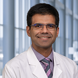 Dr. Mohammad Zahid wearing a grey shirt with a stiped tie and a white lab coat standing in the Clements University Hospital lobby
