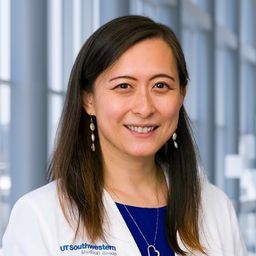 Dr. Tian Zhang wearing a dark blue shirt and a white lab coat standing in the Clements University Hospital lobby
