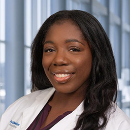 Dr. Temitayo Adegoke wearing a brown shirt, and a white lab coat standing in the Clements University Hospital lobby