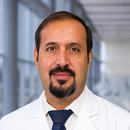 Dr. Mohammed Al Shalal wearing a white shirt with a dark patterend tie, and a white lab coat standing in the Clements University Hospital lobby