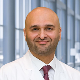 Dr. Dergham Alzubaidy wearing a white shirt with a maroon tie and a white lab coat standing in the Clements University Hospital lobby