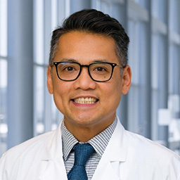 Dr. Robert Arias wearing glasses, a striped shirt with a dark tie and a white lab coat standing in the Clements University Hospital lobby