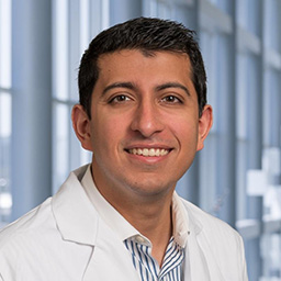 Dr. Vishal Arora wearing a striped shirt and a white lab coat standing in the Clements University Hospital lobby
