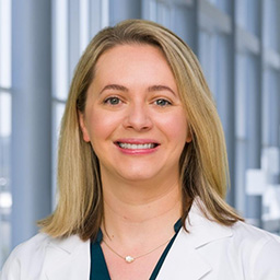 Dr. Amy Barnett wearing a dark colored shirt and a white lab coat standing in the Clements University Hospital lobby