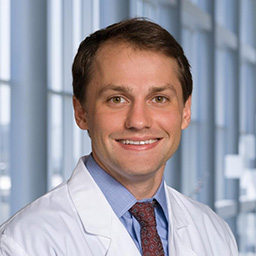 Dr. Bryan Block wearing a green blue shirt with a patterned maroon tie and a white lab coat standing in the Clements University Hospital lobby