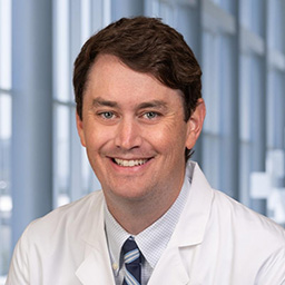 Dr. Sean Burke wearing a pin striped shirt with a striped blue tie and a white lab coat standing in the Clements University Hospital lobby