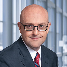 Dr. Christopher Chaney wearing dark suit, white shirt with red and blue striped tie and a white lab coat standing in the Clements University Hospital lobby