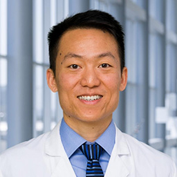 Dr. Eric Chang wearing a blue shirt with blue stiped tie and a white lab coat standing in the Clements University Hospital lobby