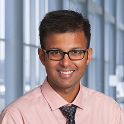 Dr. Rohan Chaubey wearing a pink shirt with a dark patterned tie and a white lab coat standing in the Clements University Hospital lobby