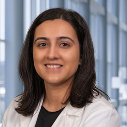 Dr. Jui Desai wearing a black shirt and a white lab coat standing in the Clements University Hospital lobby