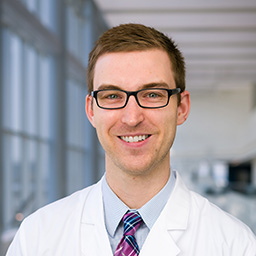 Dr. Brian Duffy wearing glasses, a light blue shirt with a red and blue plaid tie, and a white lab coat standing in the Clements University Hospital lobby