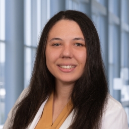 Dr. Hillary Evans wearing a tan shirt, and a white lab coat standing in the Clements University Hospital lobby