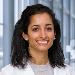 Dr. Anita Hegde wearing a green shirt, and a white lab coat standing in the Clements University Hospital lobby