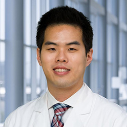 Dr. Michael Hwang wearing a white shirt with a colorful plaid tie, and a white lab coat standing in the Clements University Hospital lobby