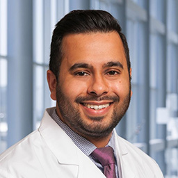 Dr. Denny Jacob wearing a blue shirt with a purlple tie and a white lab coat standing in the Clements University Hospital lobby