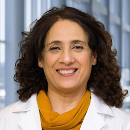 Dr. Syeda Jaffery wearing an ocher shirt, and a white lab coat standing in the Clements University Hospital lobby