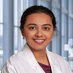 Dr. Sana Khaliq wearing a maroon shirt, and a white lab coat standing in the Clements University Hospital lobby