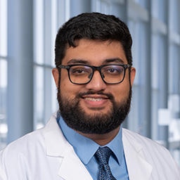 Dr.
Sharan Krishnan wearing a blue shirt with a dark blue necktie and a white lab coat standing in the Clements University Hopsital lobby