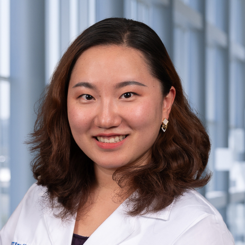 Dr. Mozhu Li wearing a dark shirt, and a white lab coat standing in the Clements University Hospital lobby