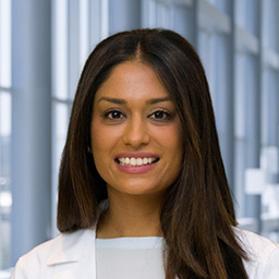 Dr. Hina Mehta wearing a light blue shirt, and a white lab coat standing in the Clements University Hospital lobby