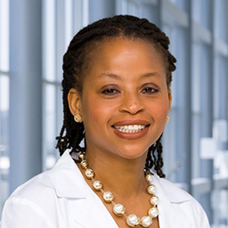 Dr. Kehinde Odedosu wearing a string of pearls and a white lab coat standing in the Clements University Hospital lobby