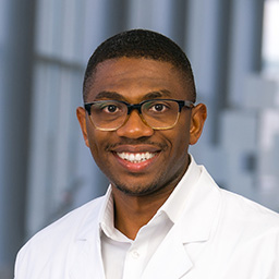 Dr. Olufolarin Oke wearing a white shirt and a white lab coat standing in the Clements University Hospital lobby