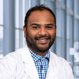 Dr. Achint Patel wearing a blue checkard shirt and a white lab coat standing in the Clements University Hospital lobby