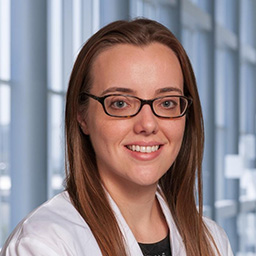 Dr. Lindsay Ripley wearing glasses, a dark shirt, and a white lab coat standing in the Clements University Hospital lobby