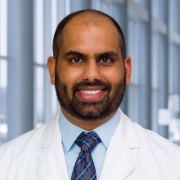 Dr. Nainesh Shah wearing glasses, a light blue shirt with a striped tie and a white lab coat standing in the Clements University Hospital lobby