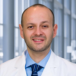 Dr. Jose Soto wearing a blue shirt with a blue striped tie and a white lab coat standing in the Clements University Hospital lobby
