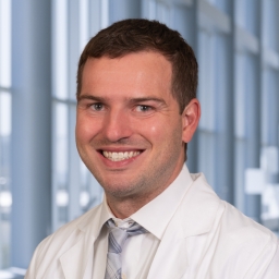 Dr. Theo Sottero wearing a white shirt with a grey striped tie and a white lab coat standing in the Clements University Hospital lobby