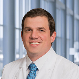 Dr. Jason Wagner wearing a white shirt with a bright blue tie, and a white lab coat standing in the Clements University Hospital lobby