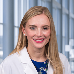 Dr. Averi E. White wearing a blue floral shirt, and a white lab coat standing in the Clements University Hospital lobby