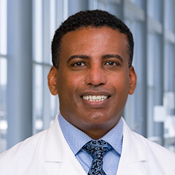 Dr. Libay Woldeyes wearing a blue shirt with a blue patterned tie and a white lab coat standing in the Clements University Hospital lobby