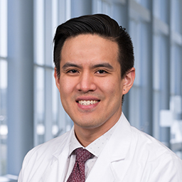 Dr. Andrew Yu wearing a green white shirt with a maroon tie, and a white lab coat standing in the Clements University Hospital lobby