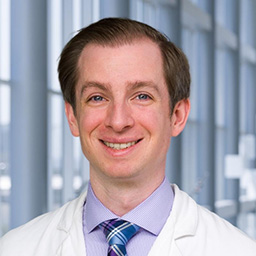 Dr. James Zasadzinski wearing a lavender shirt with a plaid tie and a white lab coat standing in the Clements University Hospital lobby