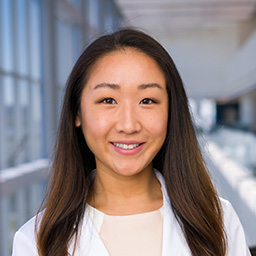 Dr. Dawn Zhao wearing a beige shirt, and a white lab coat standing in the Clements University Hospital lobby
