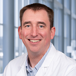 Dr. James Colbert wearing a blue and white striped shirt and a white lab coat