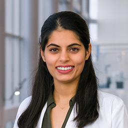 Dr. Nabeeha Ahmad wearing a gray shirt, and a white lab coat standing in the Clements University Hospital lobby