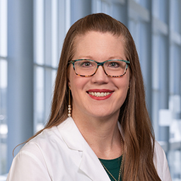 Dr. Jaclyn Albin wearing glasses, a green shirt, and a white lab coat standing in the Clements University Hospital lobby