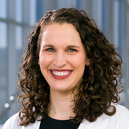 Dr. Emily Bufkin wearing a black shirt, and a white lab coat standing in the Clements University Hospital lobby