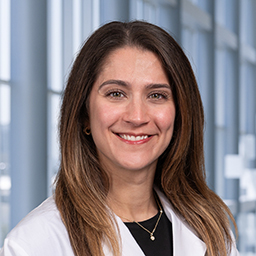 Dr. Brianna Saadat wearing a black shirt, and a white lab coat standing in the Clements University Hospital lobby