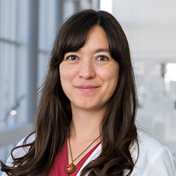 Dr. Michelle Sandoval Cabanas wearing a red shirt, and a white lab coat standing in the Clements University Hospital lobby