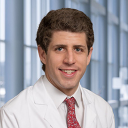Dr. Mauricio Ostrosky Frid wearing a whit shirt with a red patterned tie and a white lab coat standing in the Clements University Hospital lobby